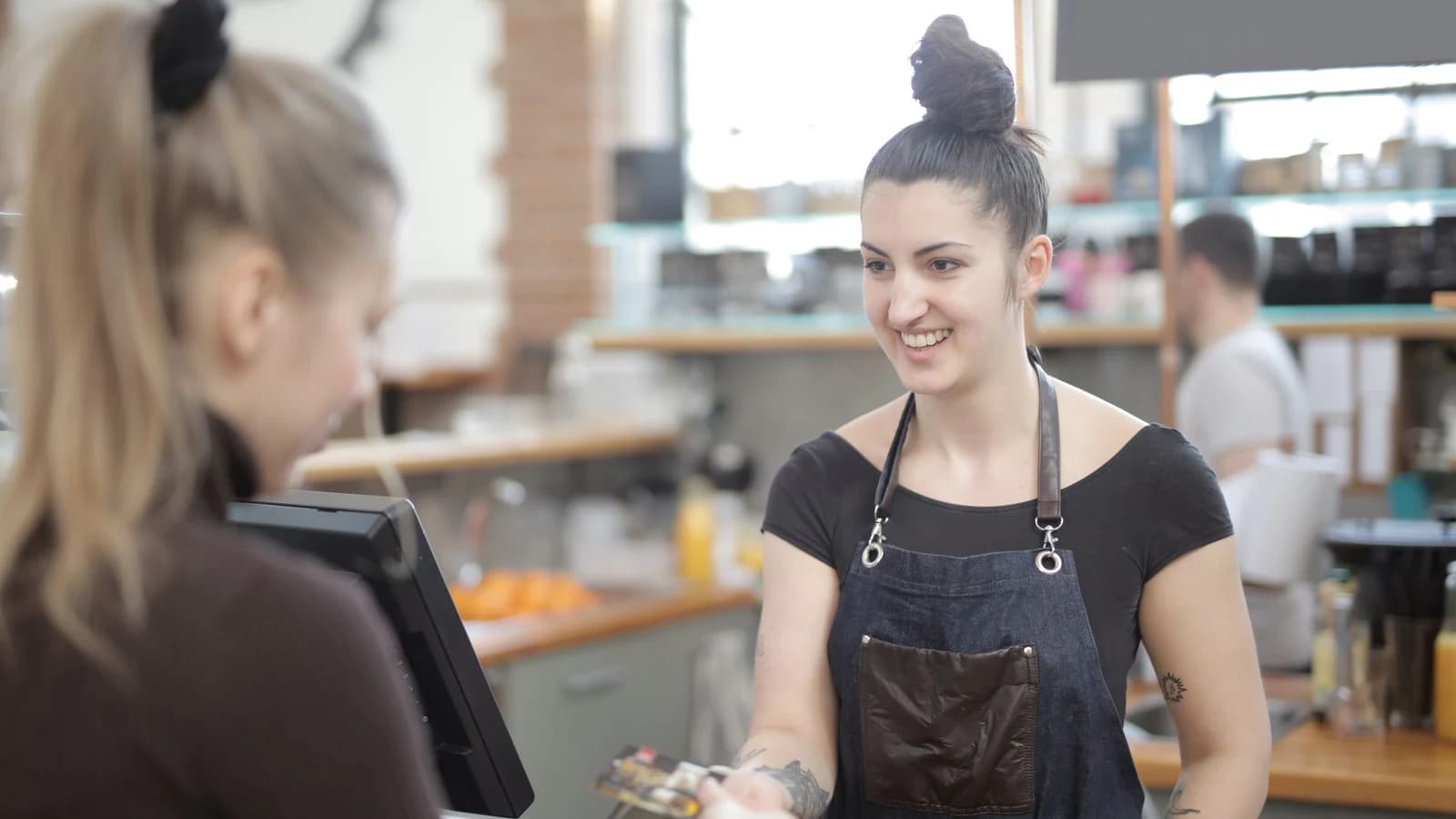 A cafe customer making a card payment while a barista holds the payment terminal
