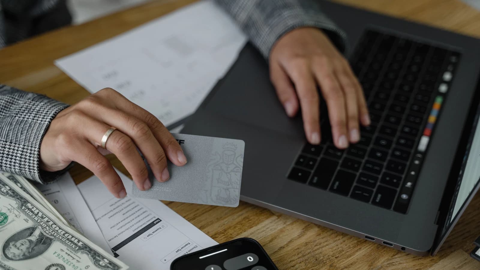 A person holding a credit card beside a laptop, cash and calculator while reviewing finances