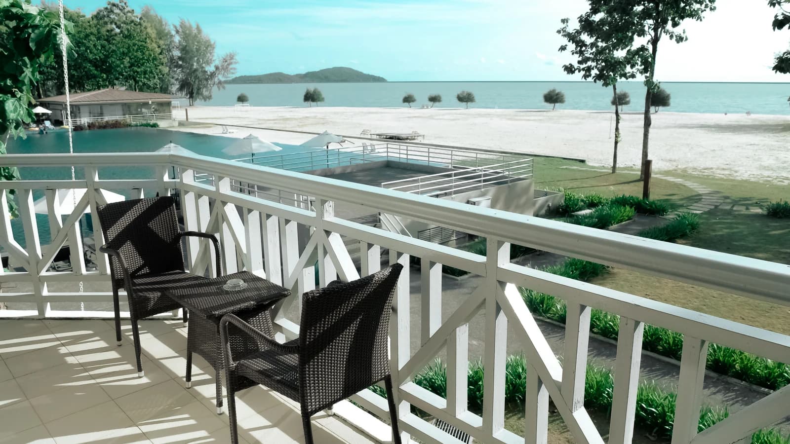 Wicker chairs on a balcony overlooking an ocean and pool