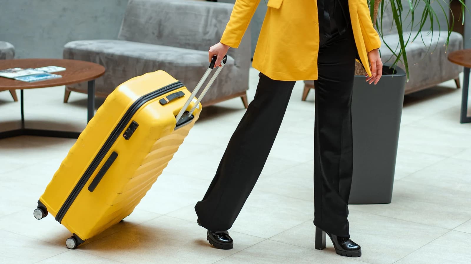 Traveler in a yellow coat pulling a yellow suitcase through a hotel lobby