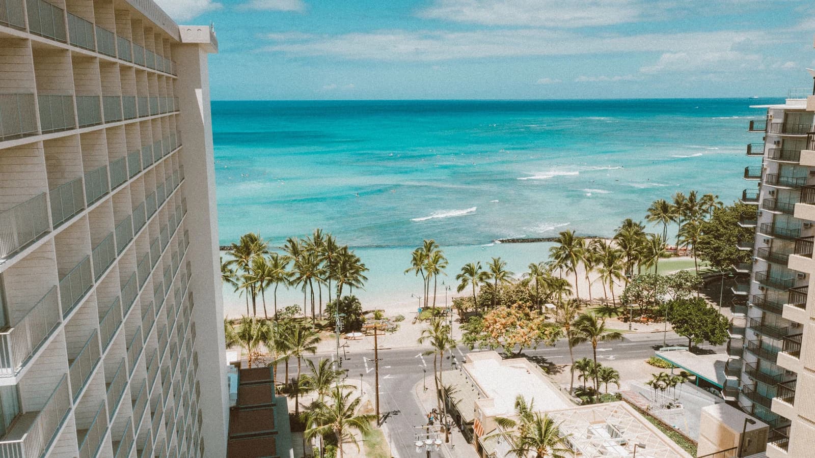 A sunny view of Waikiki Beach, palm trees and oceanfront buildings from a hotel balcony in Honolulu