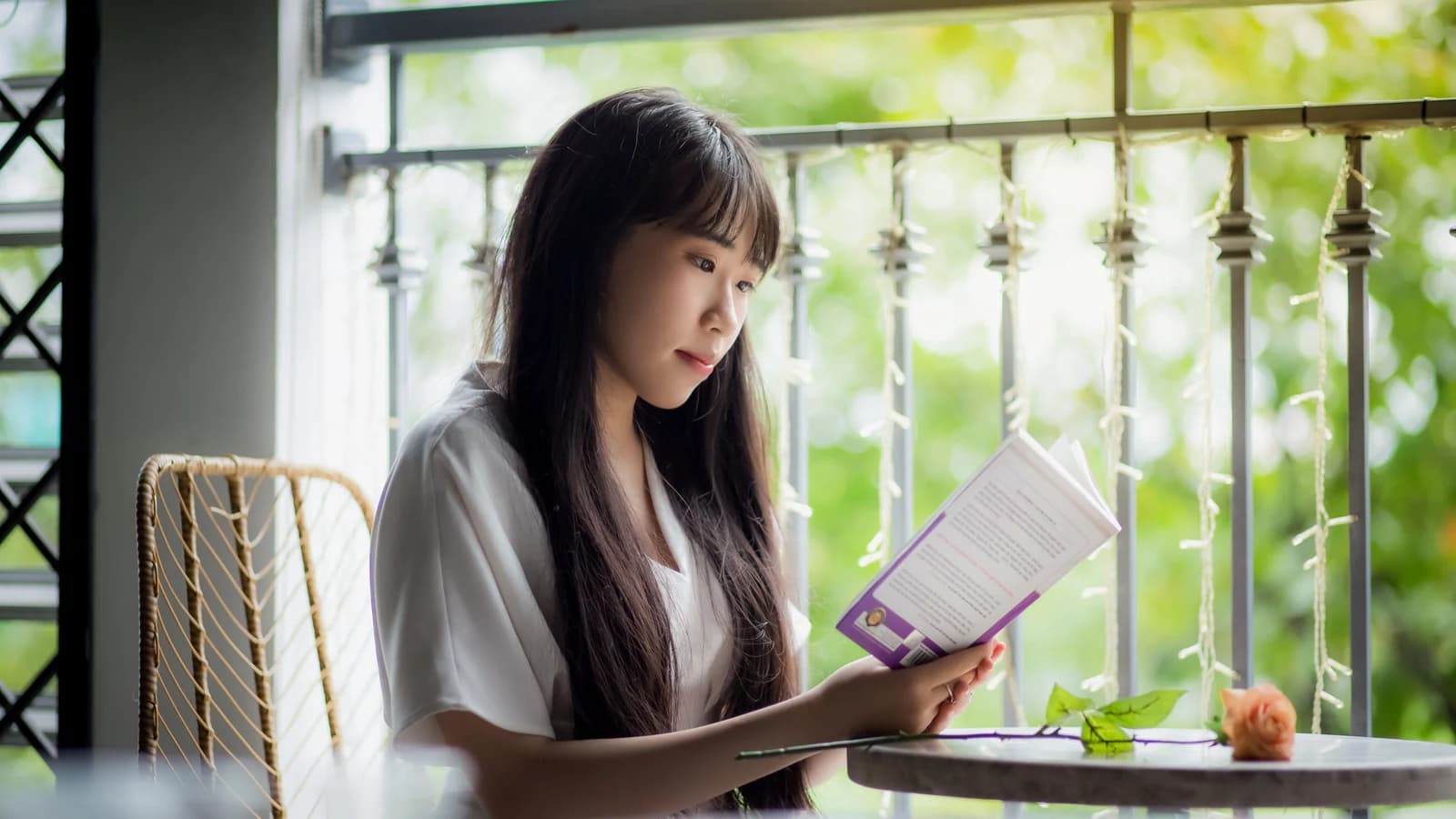Woman reading a book on a sunny balcony surrounded by greenery