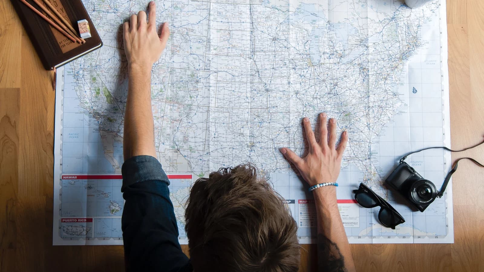 Traveler examining a paper map at home with a camera and coffee nearby