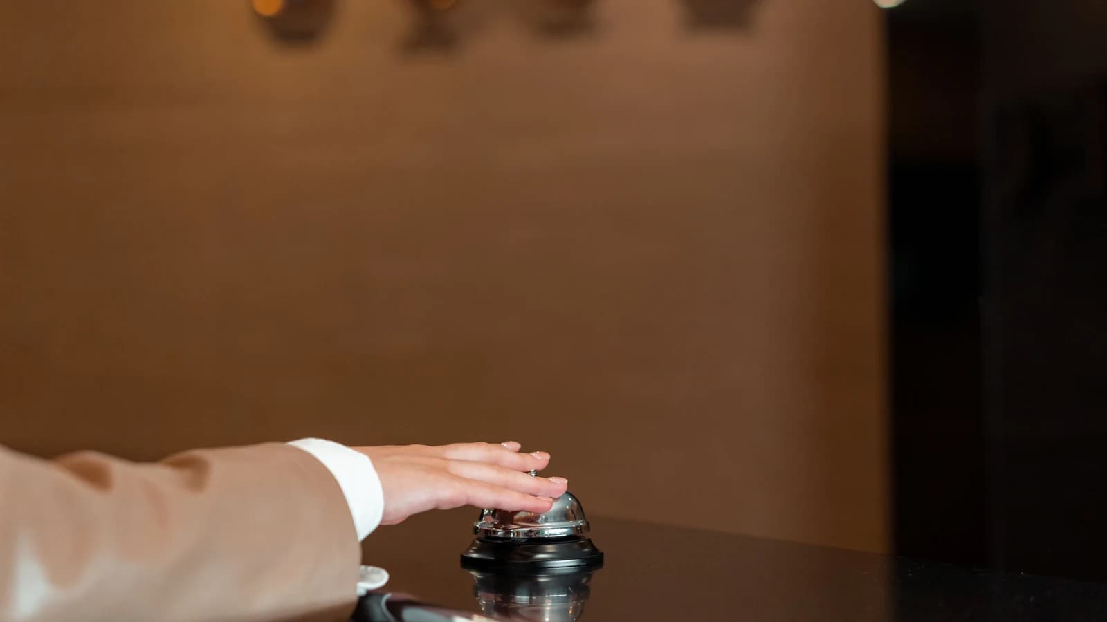 A guest's hand pressing a service bell at a hotel reception counter