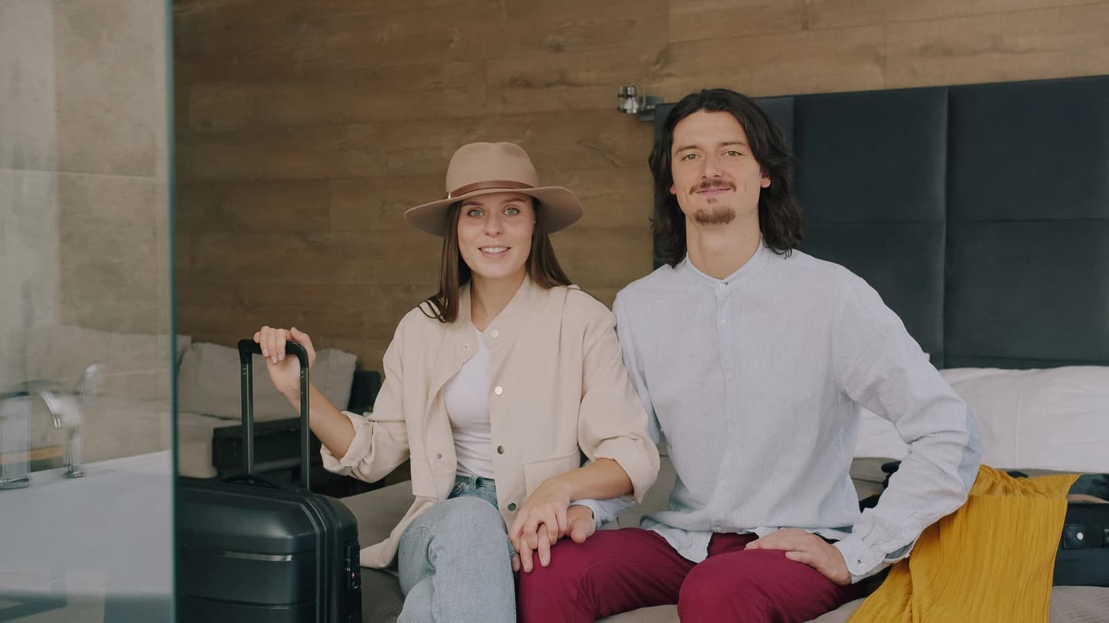 A young couple sitting in a hotel room beside their luggage